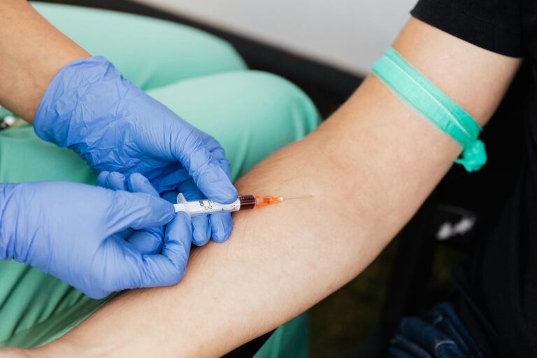 Healthcare worker drawing blood from patient's arm with syringe.